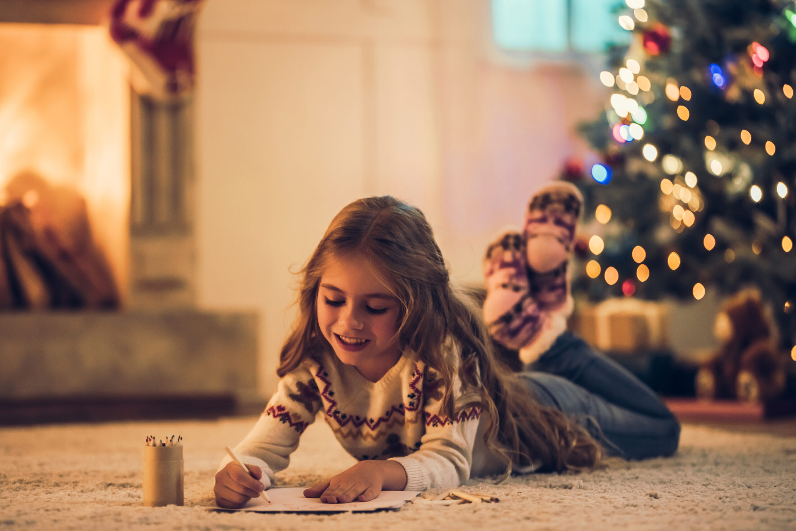 Child writing by Christmas tree and fireplace