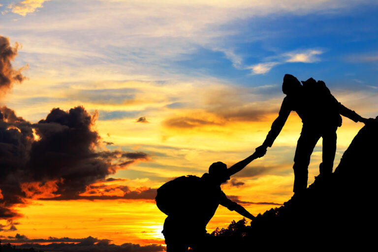 Silhouettes of hikers helping each other at sunset.
