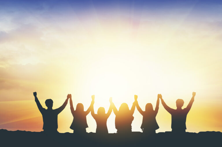 Silhouetted group celebrating against sunrise.