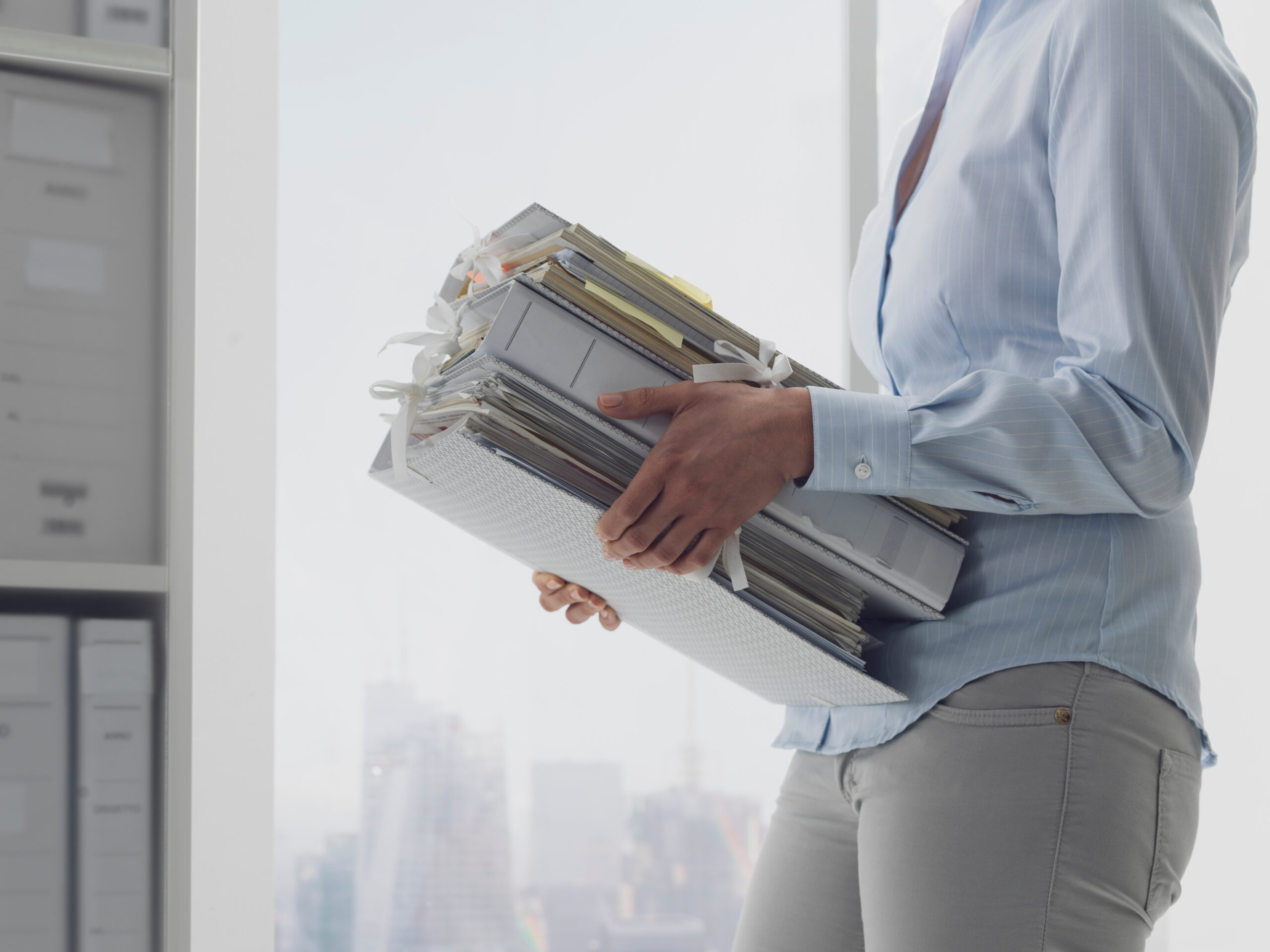 Person carrying binders and papers in office.