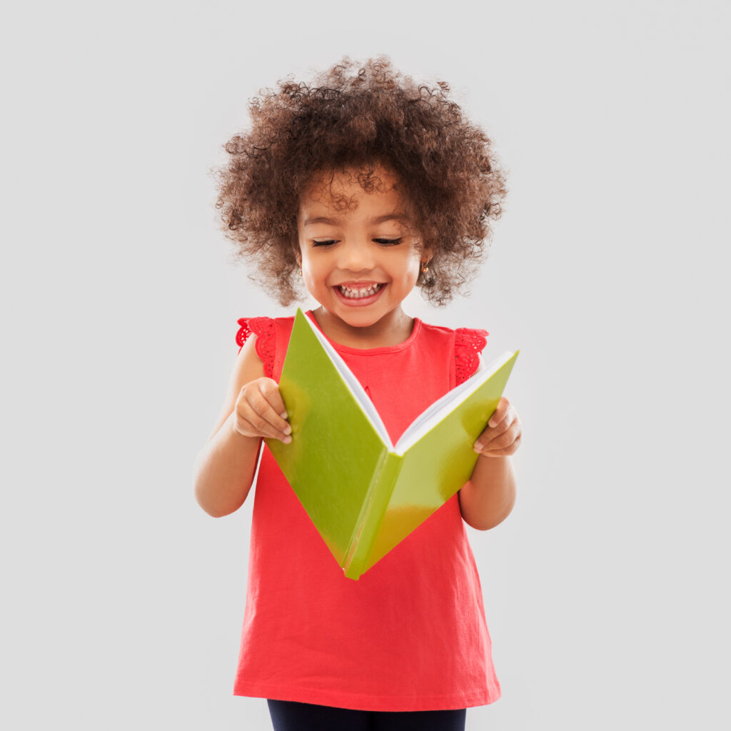 Child reading a green book, smiling joyfully.
