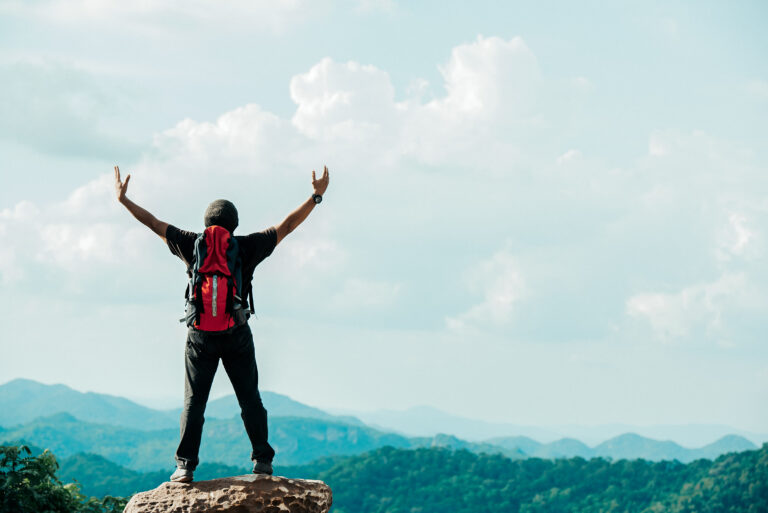 Person celebrating atop a mountain with backpack.