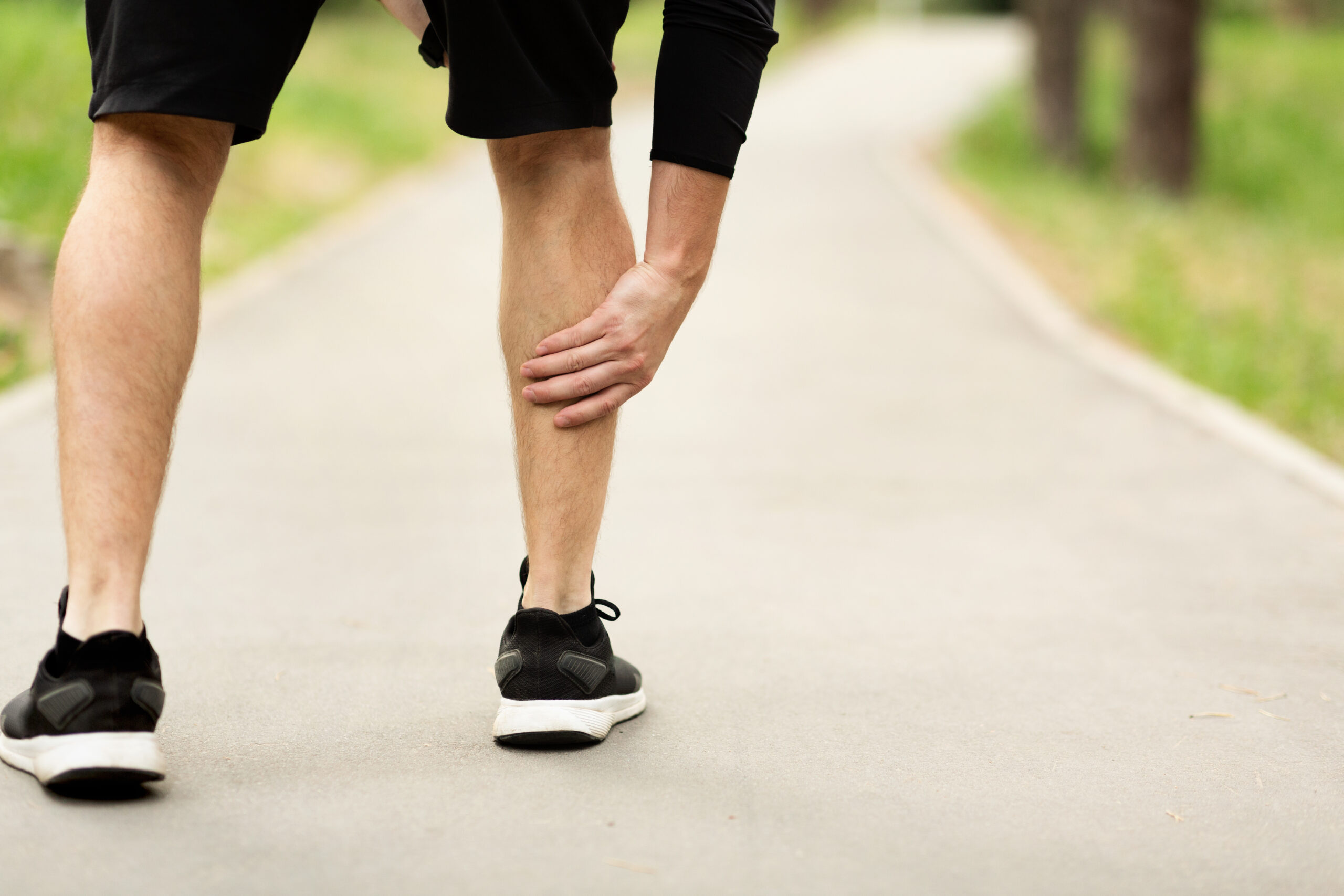 Runner holding calf muscle on path