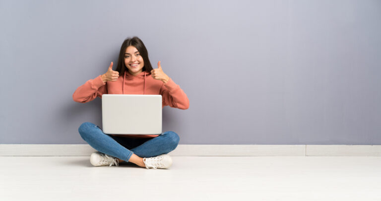 Cheerful person giving thumbs up with laptop