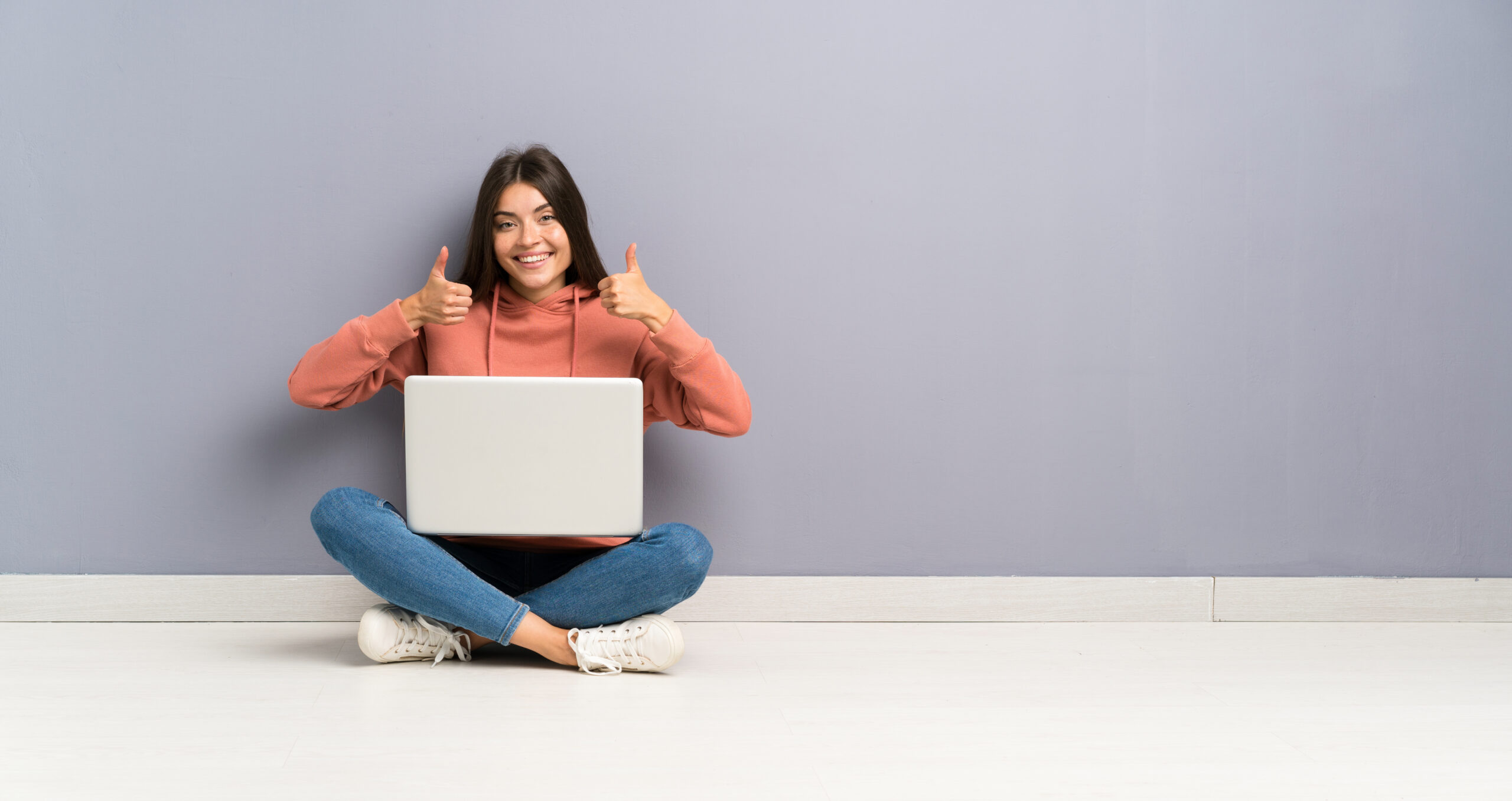 Cheerful person giving thumbs up with laptop