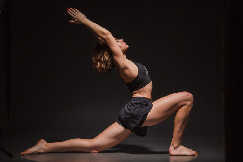 Person performing yoga lunge pose on dark background.