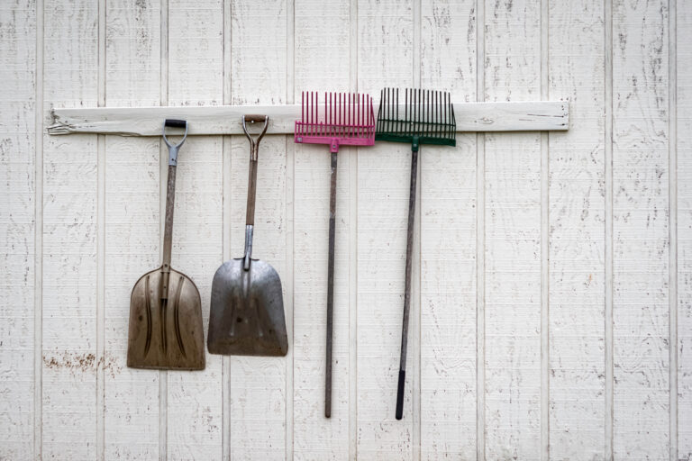 Four garden tools hanging on wooden wall