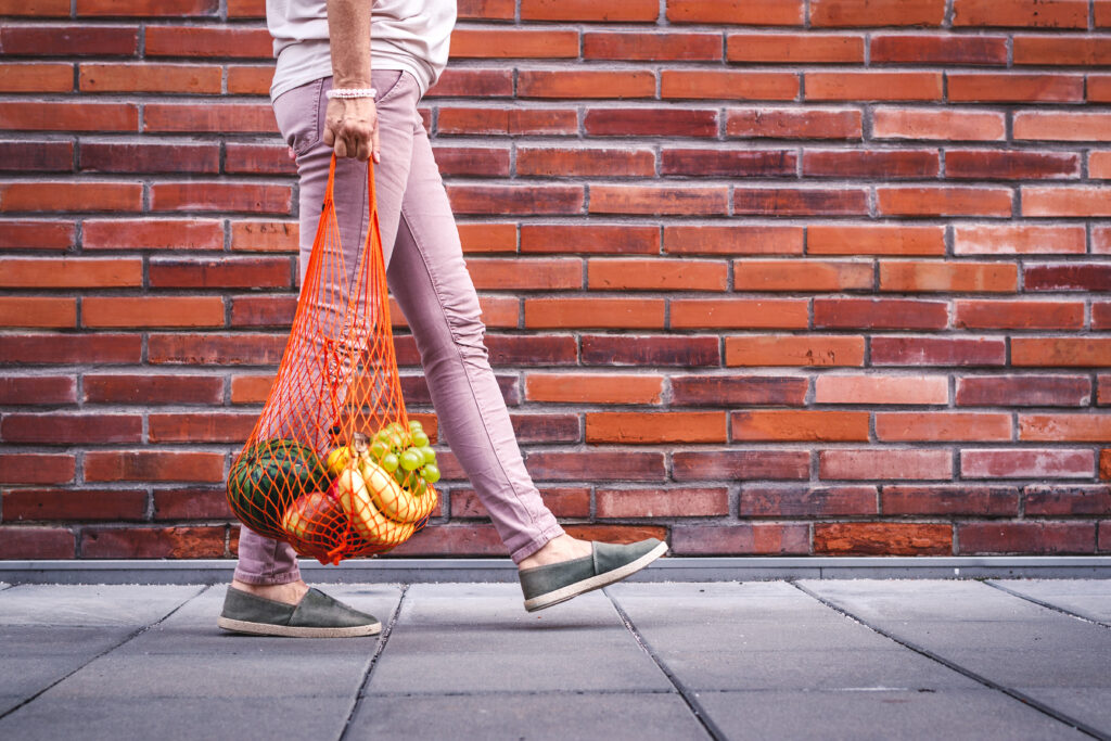 Person walking with mesh grocery bag of fruit.