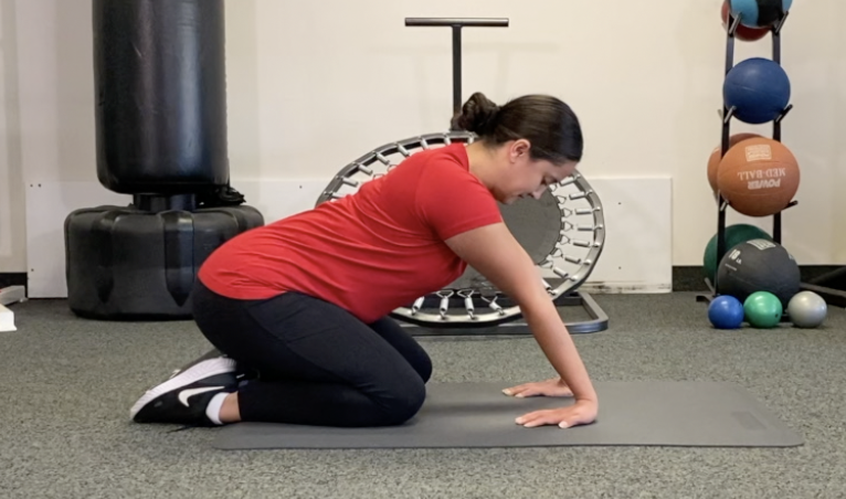 Woman practicing wrist stretch on mat in gym.